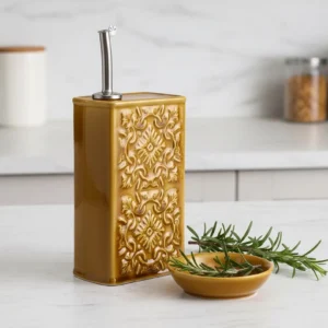 Un huilier AZULEJO ocre en céramique posé sur un comptoir à côté d'une coupelle et de brins de romarin.