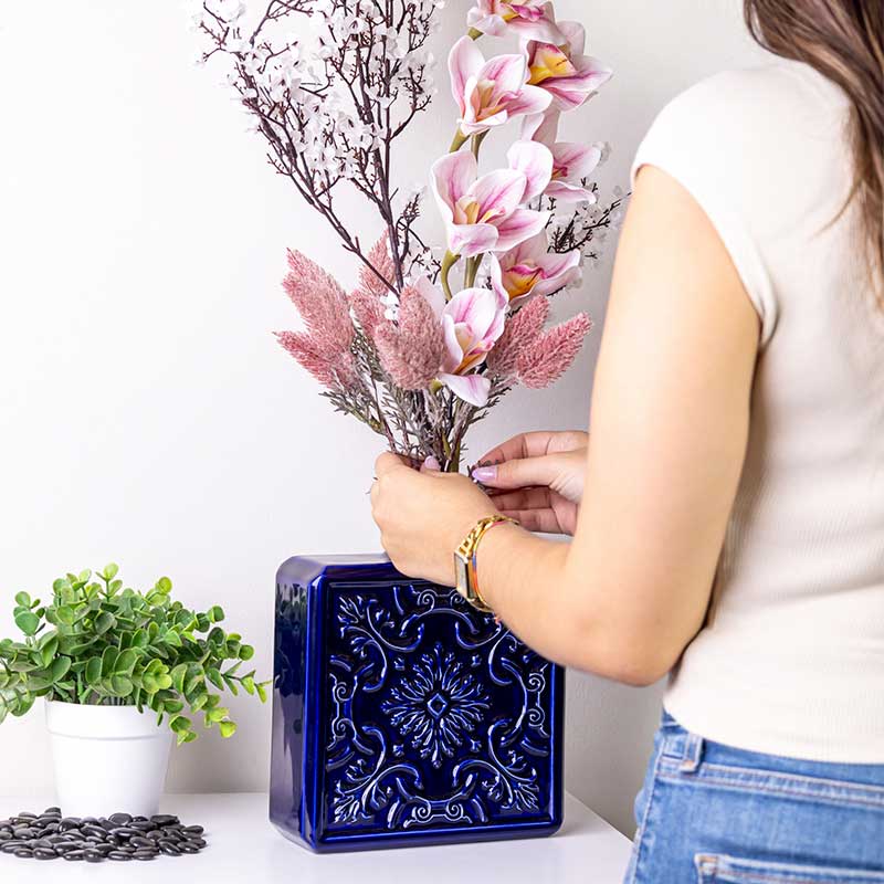 Un grand vase AZULEJO bleu en céramique dans lequel une femme arrange un bouquet de fleurs roses et blanches.